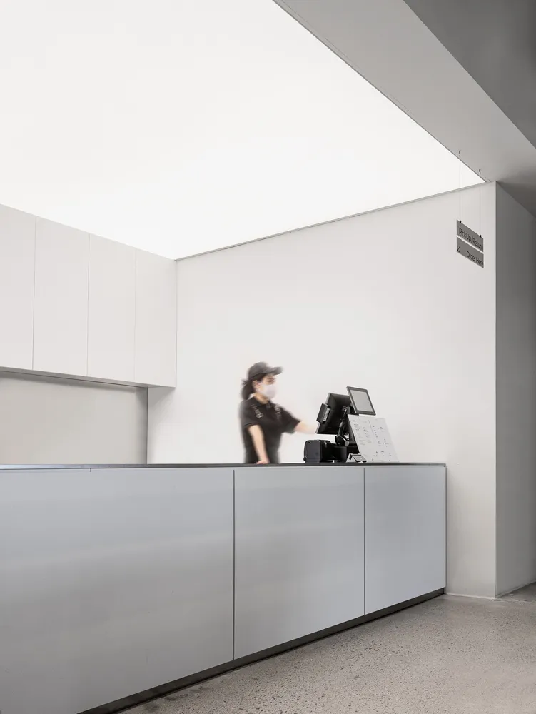 A minimalist modern reception counter with a concrete and white surface, featuring a digital display and a person wearing a f