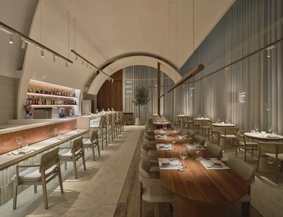 Modern restaurant interior with wooden tables, glass walls, and fabric seating.