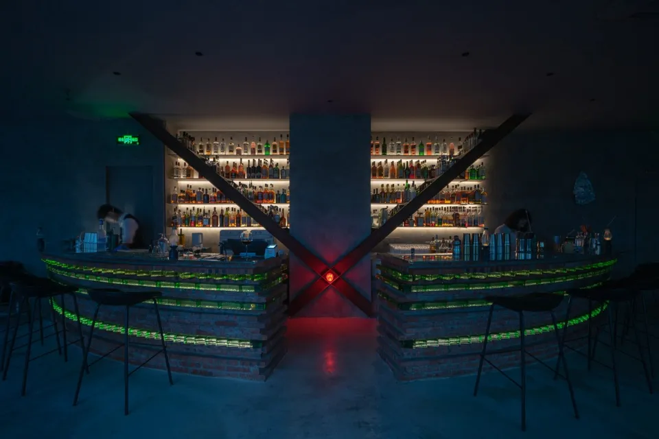 Modern bar interior with brick counter and concrete walls, illuminated by green and red lights.