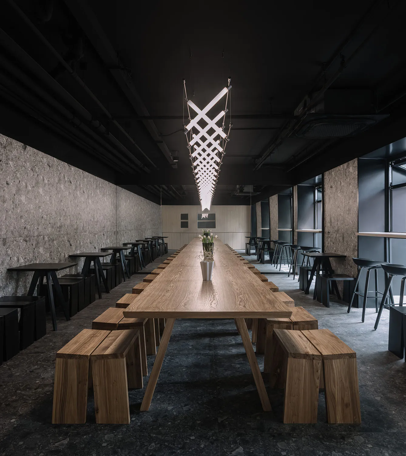Long wooden dining table with benches and stools in a modern restaurant setting.