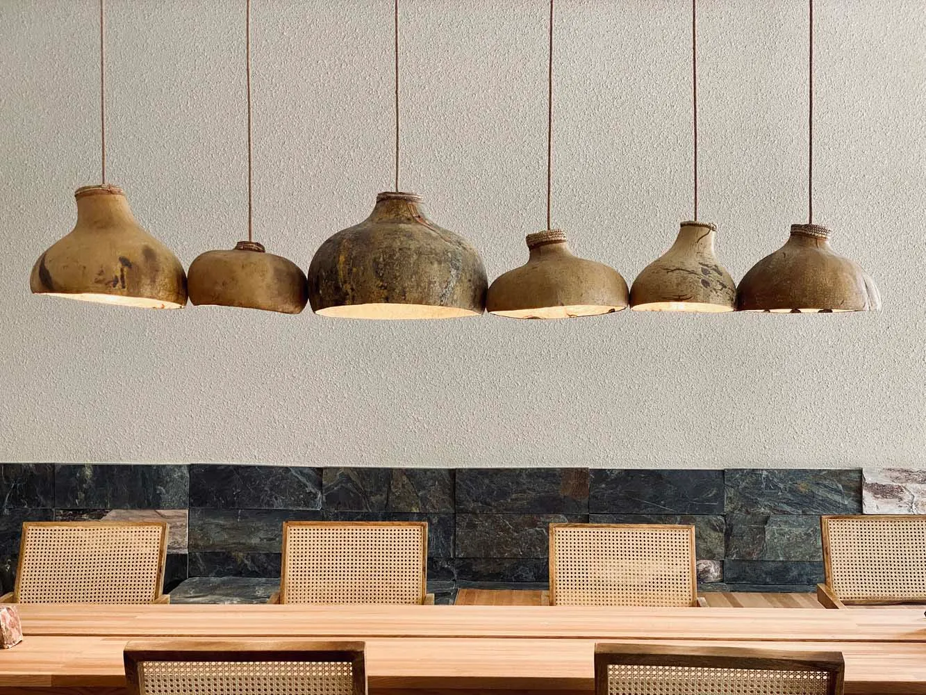 A row of rustic, handmade clay pendant lights hang above a dining table in an industrial-themed restaurant interior.