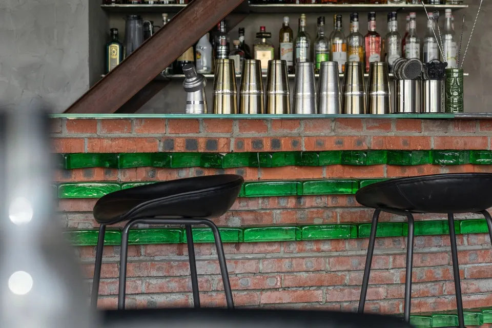 A modern bar counter made of brick, with green accents and various containers and bottles on the shelf.