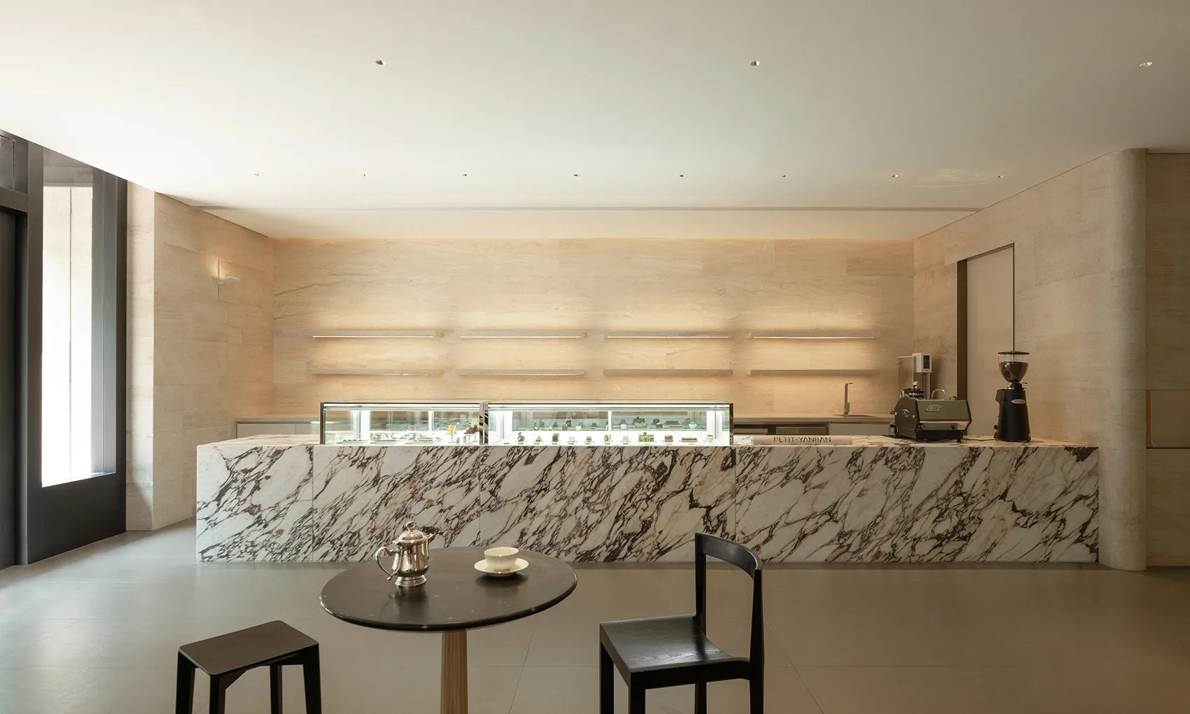 A modern cafe interior with white marble countertops, a black table, and chairs.