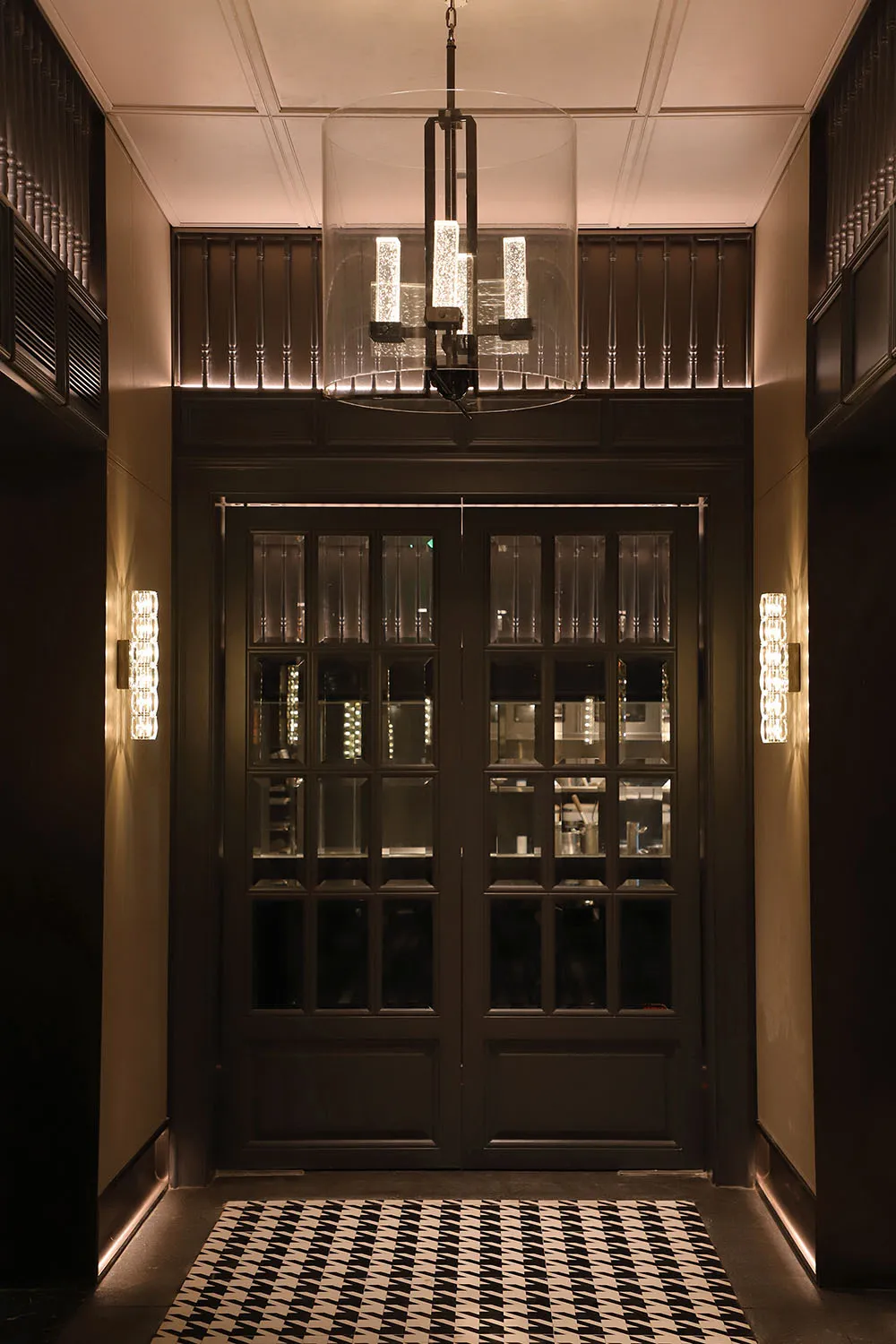 Modern entrance lobby featuring glass doors with a sleek steel frame, illuminated by contemporary lighting fixtures and a pat
