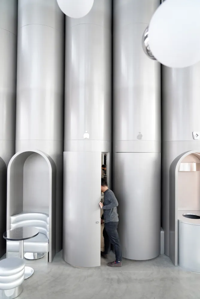A minimalist coffee shop interior with tall metal cylindrical columns and round hanging lights