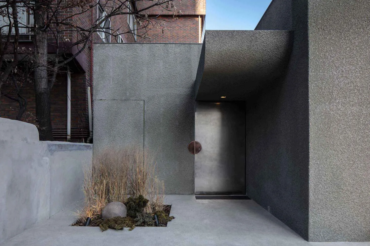 A modern concrete entranceway with a sleek, stainless-steel door and minimalist landscaping.