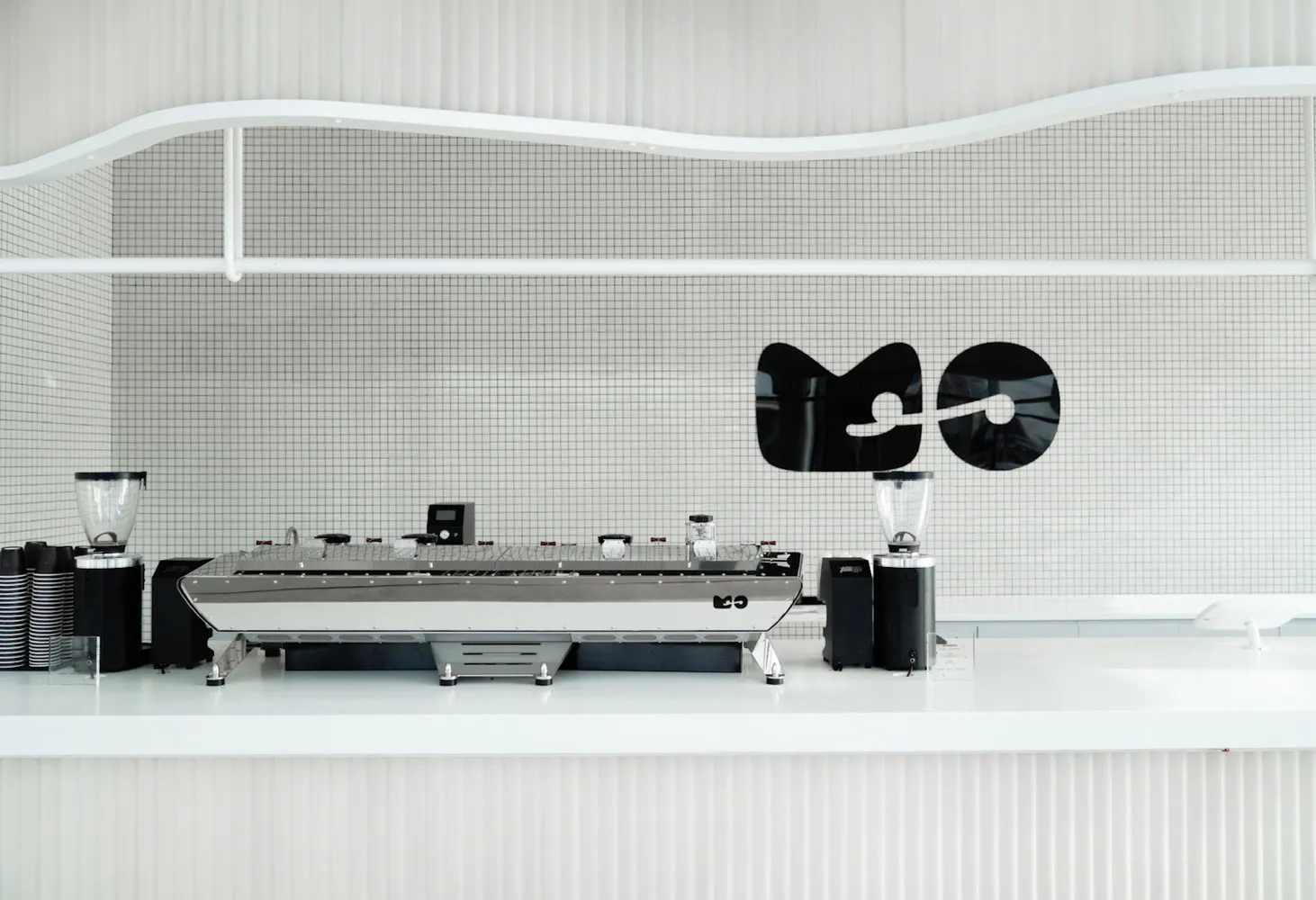 Modern minimalist coffee shop interior with sleek white surfaces and a sleek coffee machine.