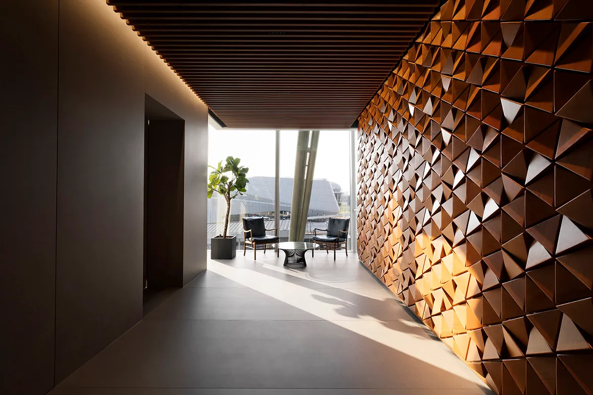 A modern office space featuring a wall made of wooden triangles and a small sitting area with chairs and a plant.