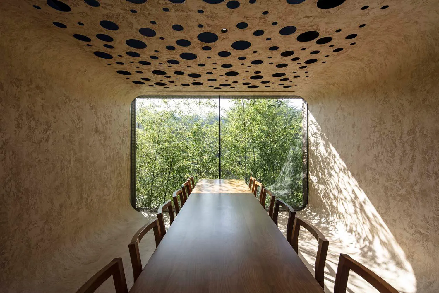 A modern dining room featuring a wooden table and chairs with a large window overlooking greenery.