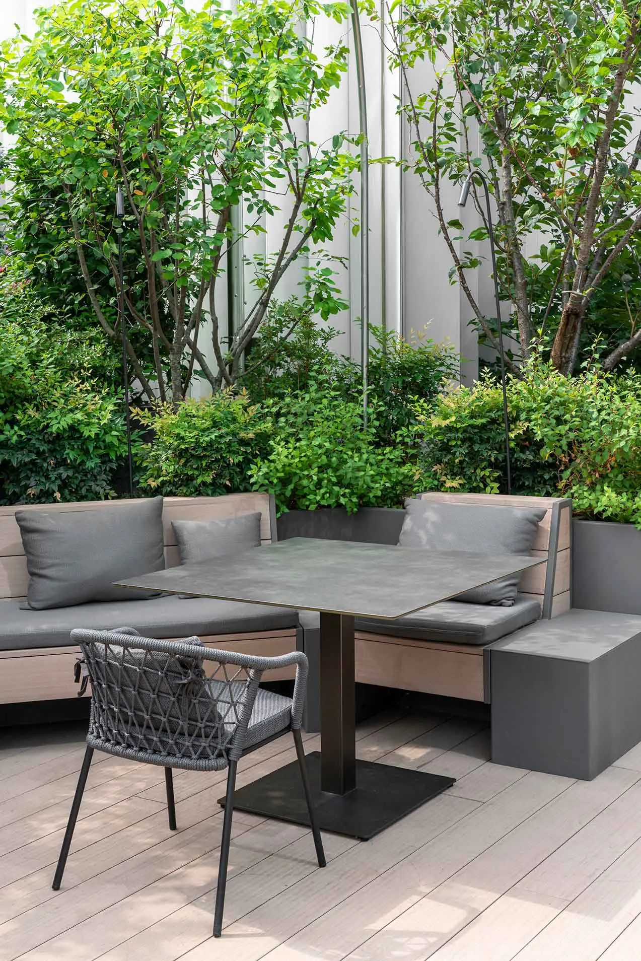 Modern outdoor garden setup featuring wooden furniture, greenery, and a square table with a metal base.