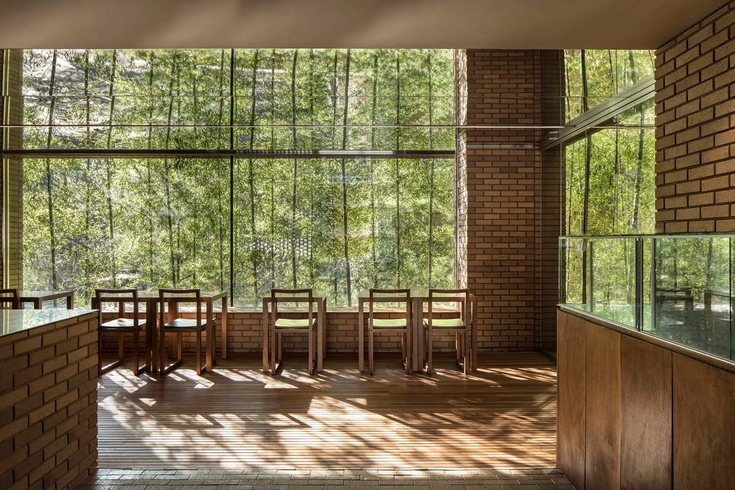 A modern coffee shop interior featuring brick walls, glass walls, and wooden furniture.