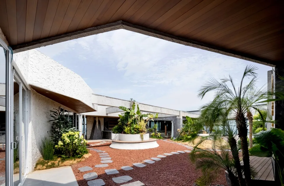 Modern residential patio with concrete floor, gravel pathway, and lush green plants.