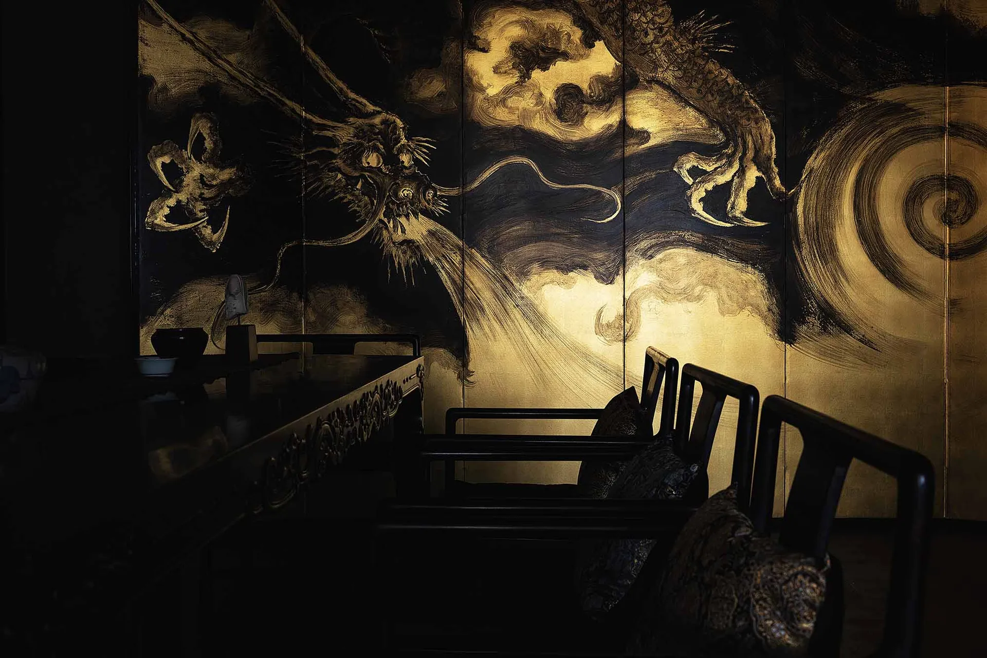 A serene living room with wooden furniture and a black and gold wood panel depicting a Chinese dragon.