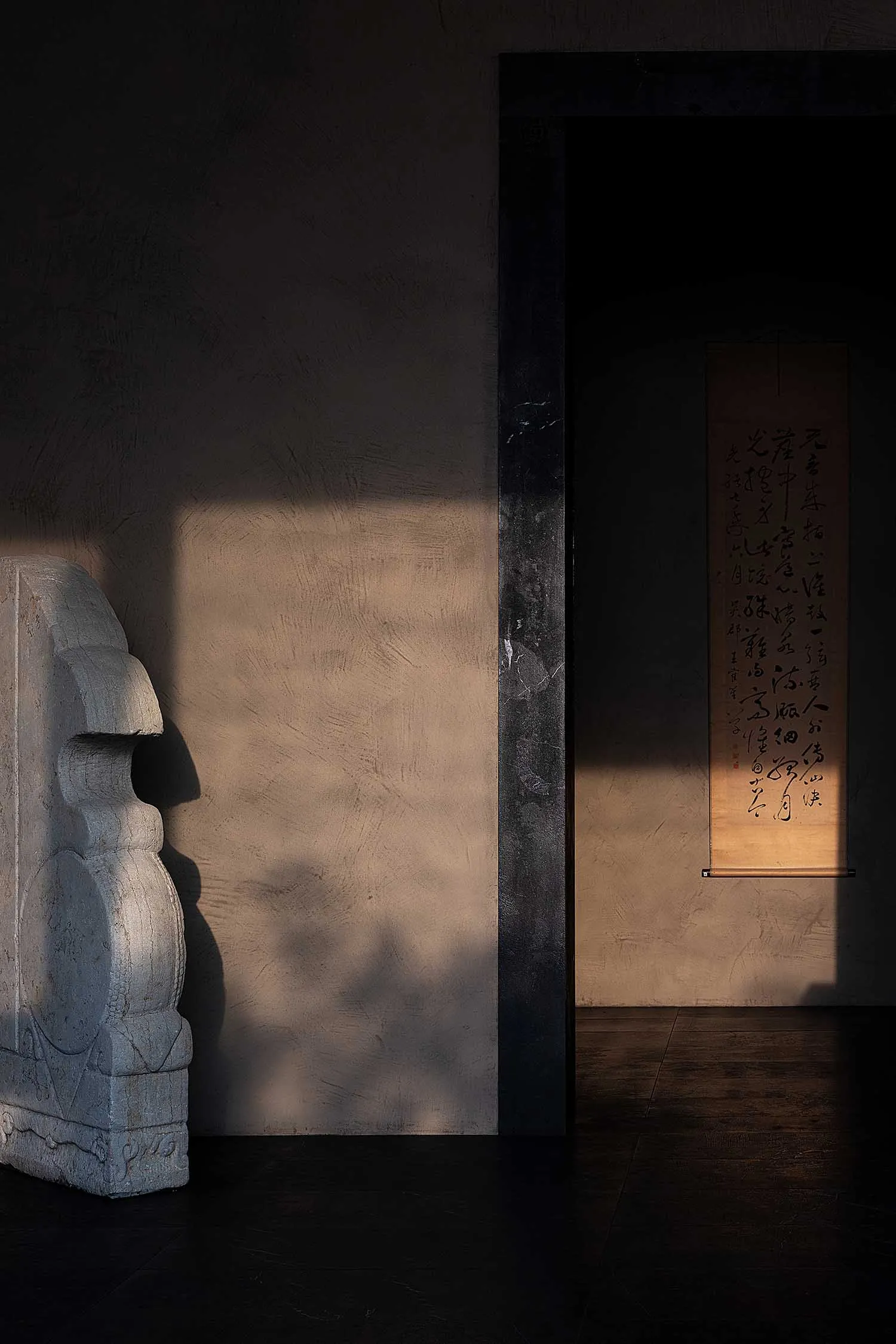 A minimalist bedroom decorated with a large concrete sculpture and a framed calligraphy scroll hanging on the wall.