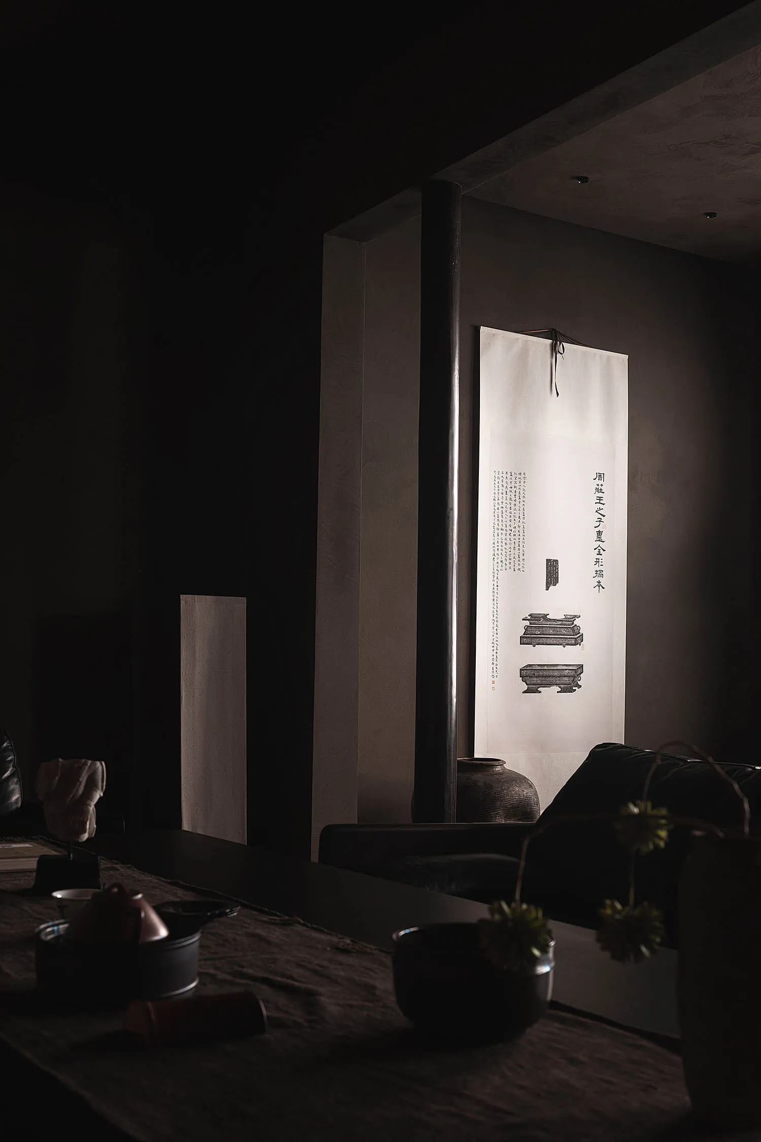 A minimalist living room with textured paper on the walls, featuring a black sofa and various decorative items.