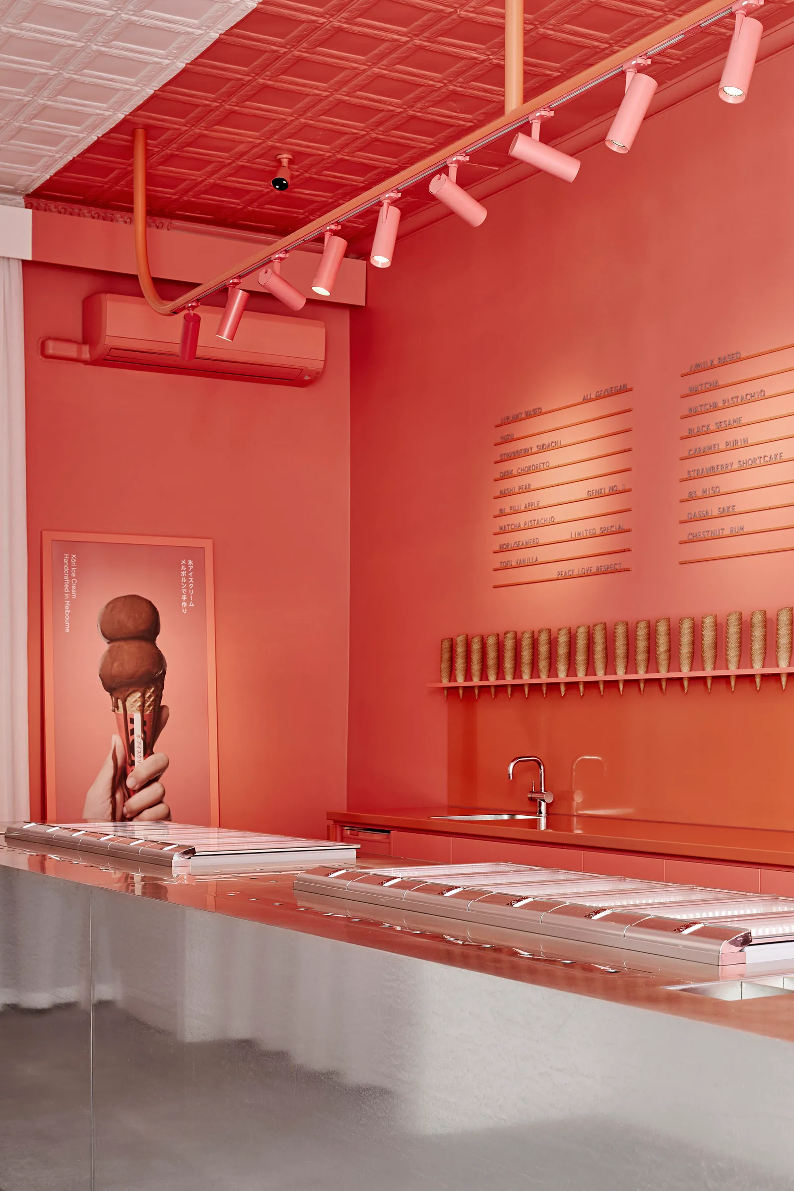 Modern restaurant interior with metallic aluminum countertop, red walls, and a menu board listing various ice cream flavors.