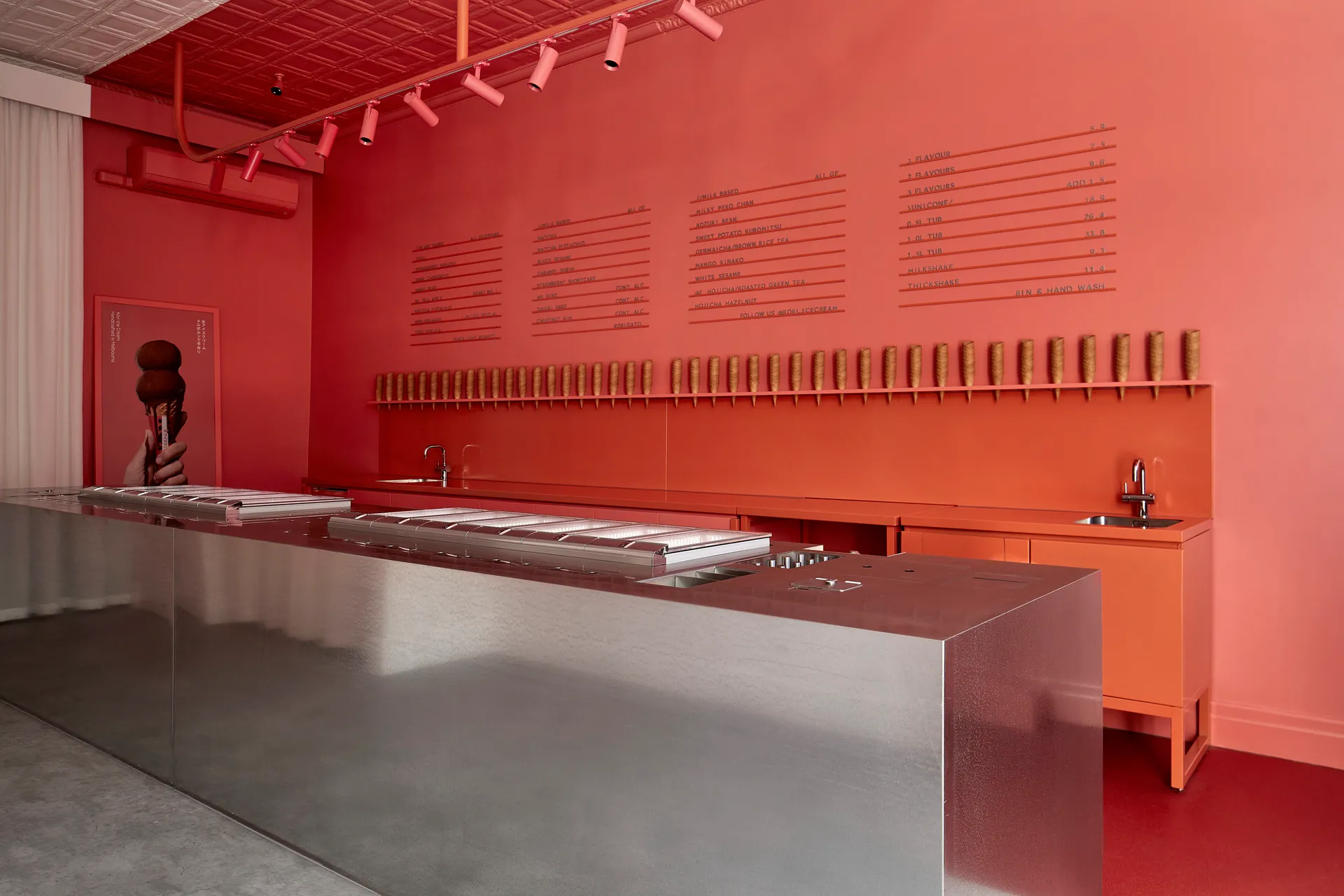 A sleek modern cafe interior with a metal counter adorned with floral print installed lights and a menu board displaying ice 