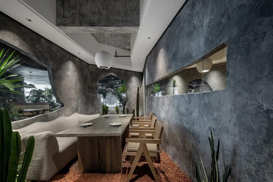 A modern minimalist restaurant interior with a concrete floor, wooden furniture, and green plants.