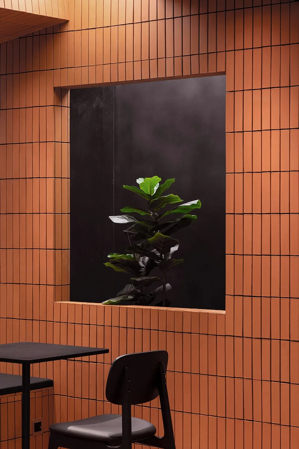 Industrial style restaurant interior featuring a black dining table and a potted plant on a window sill with orange terracott
