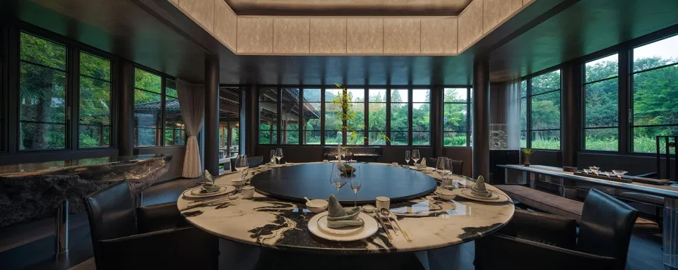 A round dining table with marble tabletop surrounded by black leather chairs, set with white plates and wine glasses.