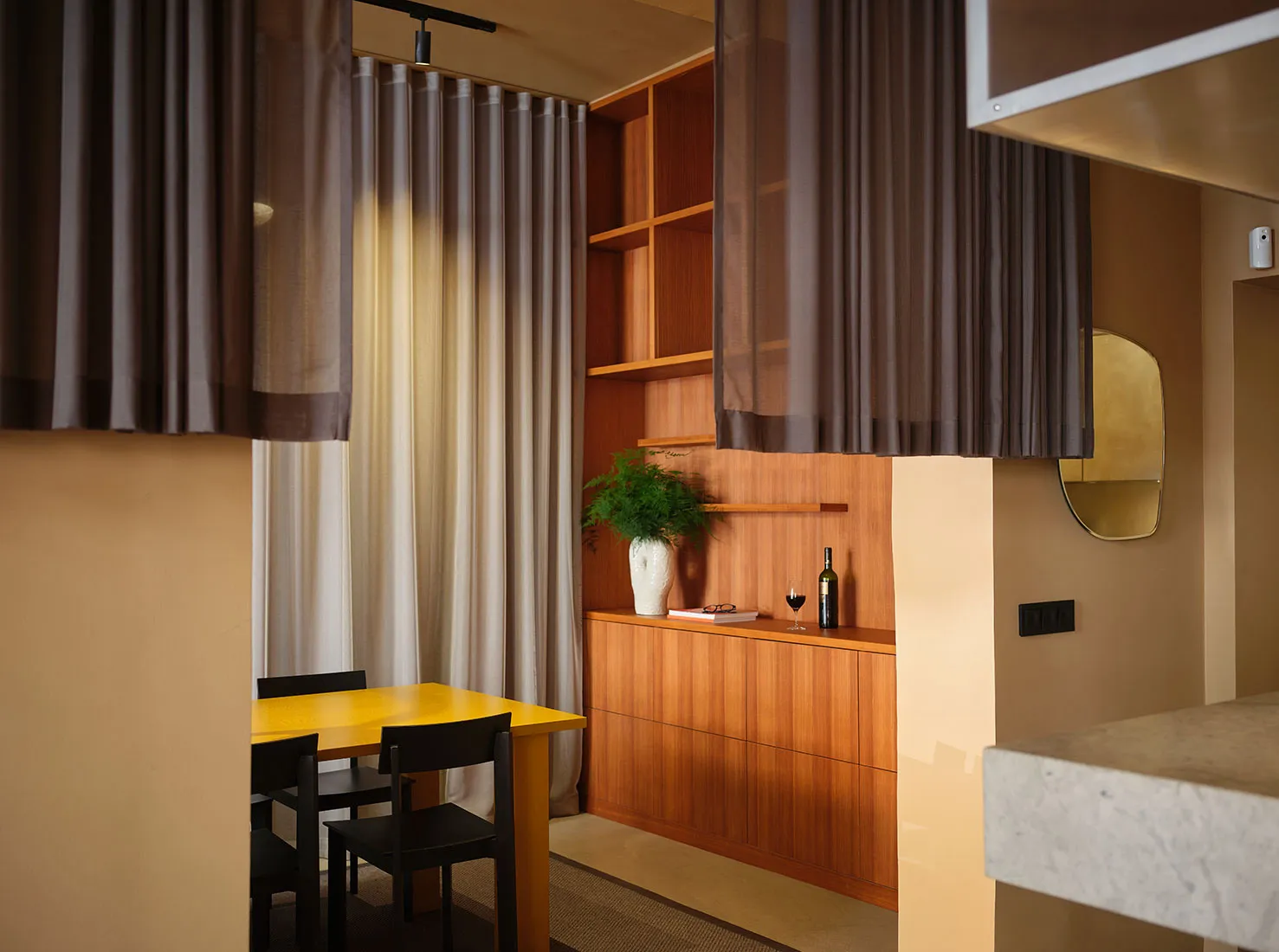 Modern apartment dining area with wooden shelves, silk curtains, and a yellow table.