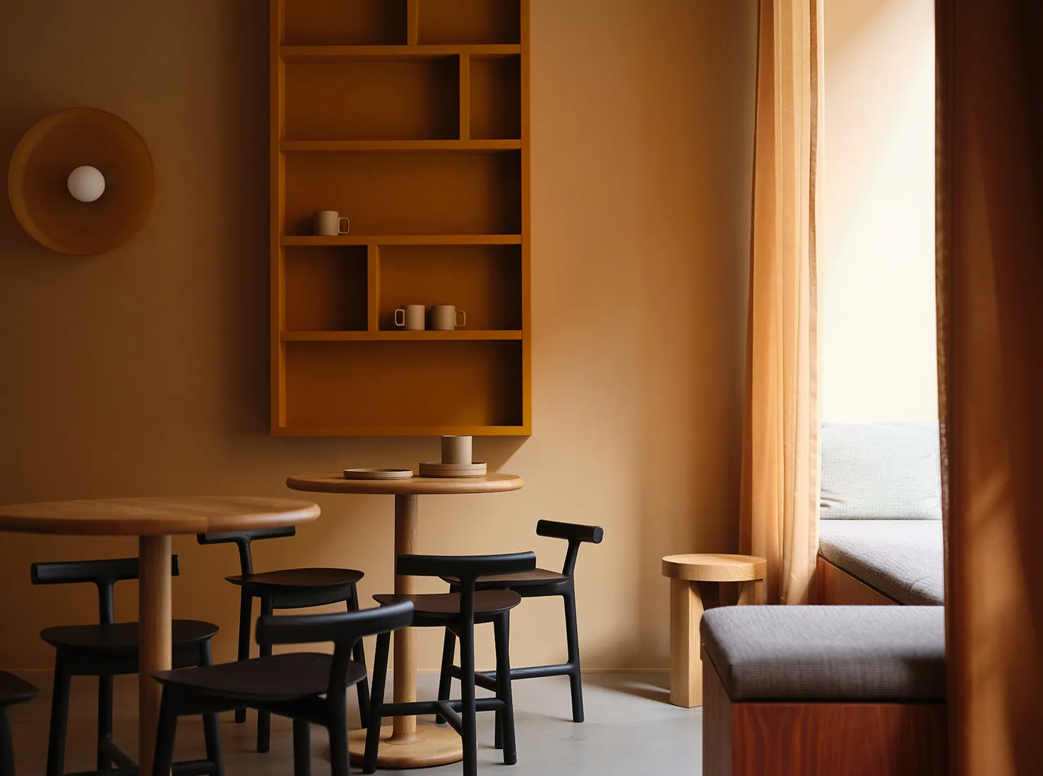 A modern cafe interior featuring wooden tables and chairs, a wooden shelf with decorative items, and a large window with curt