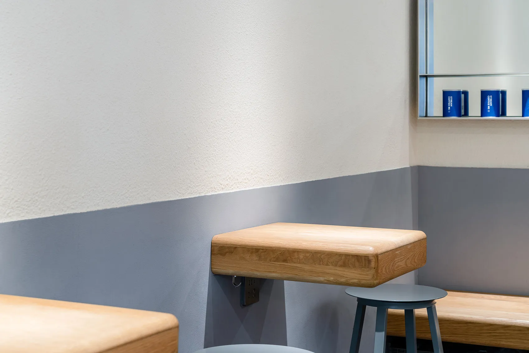 A minimalist coffee shop featuring a wooden shelf and stool, emphasizing modern design.