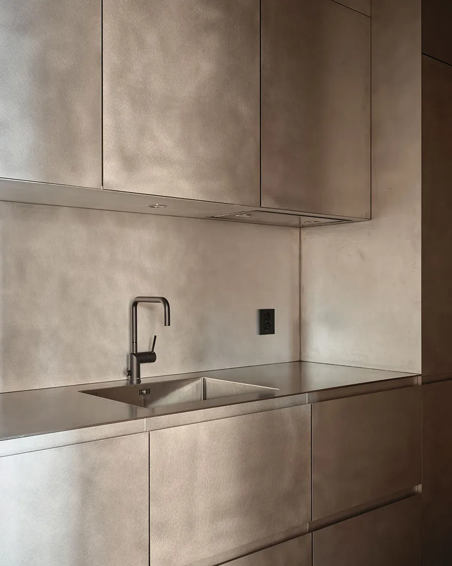 A modern, minimalist kitchen with metallic cabinets and a sleek, integrated sink.