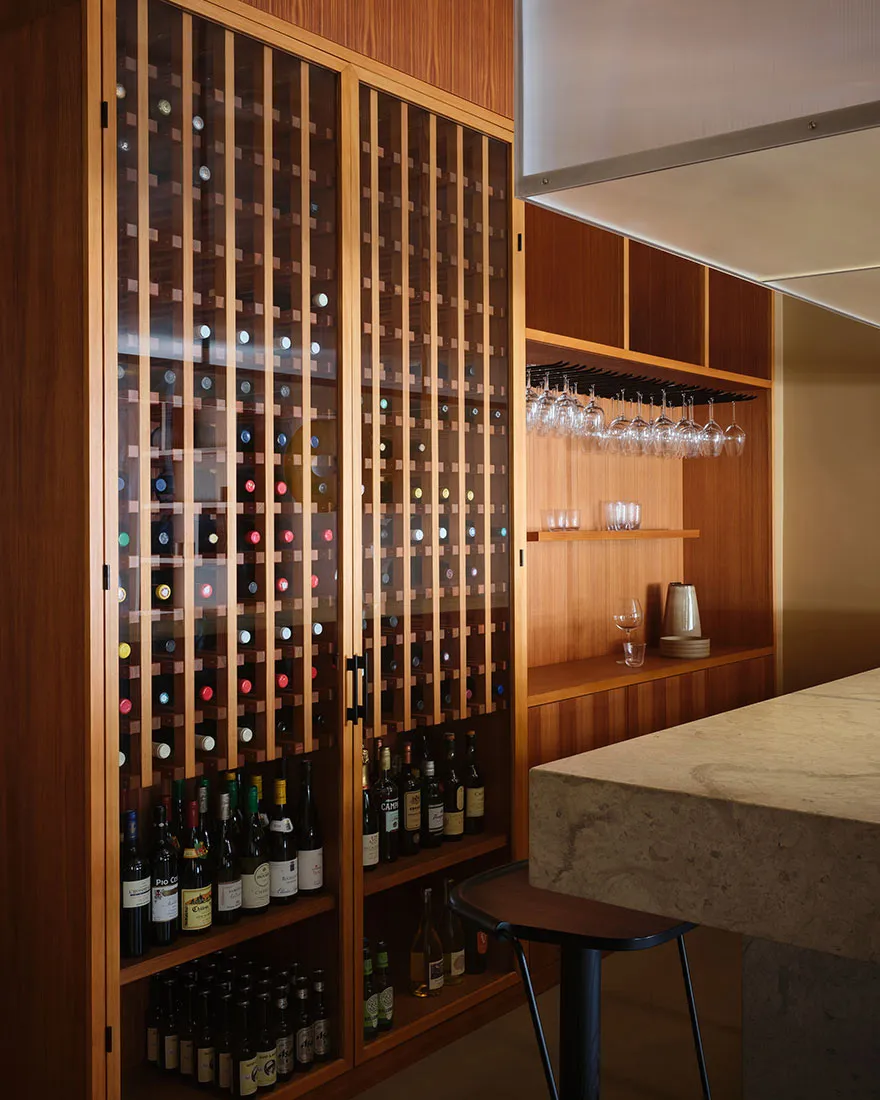 A modern restaurant bar featuring a wooden wine cabinet filled with various bottles of wine and a marble counter.