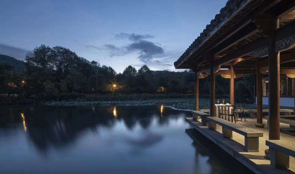 寧靜的水岸度假村,石雕映照在平靜的池塘上,周圍環繞著茂密的綠意。