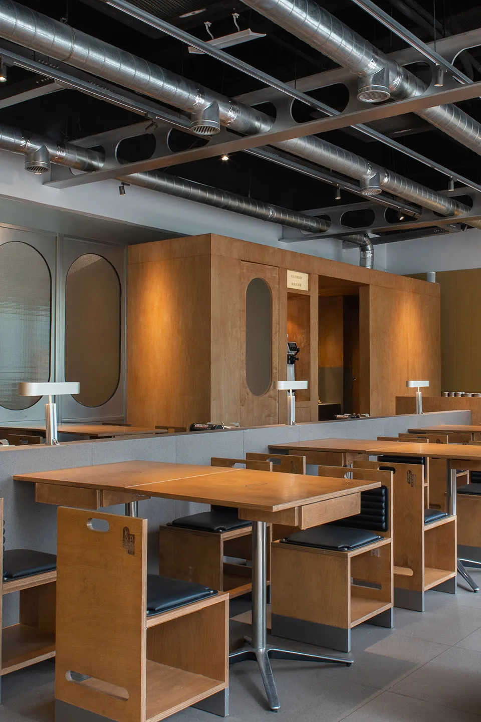 Industrial-themed cafe interior with wooden tables and chairs, under exposed ceiling with exposed pipes and lighting.