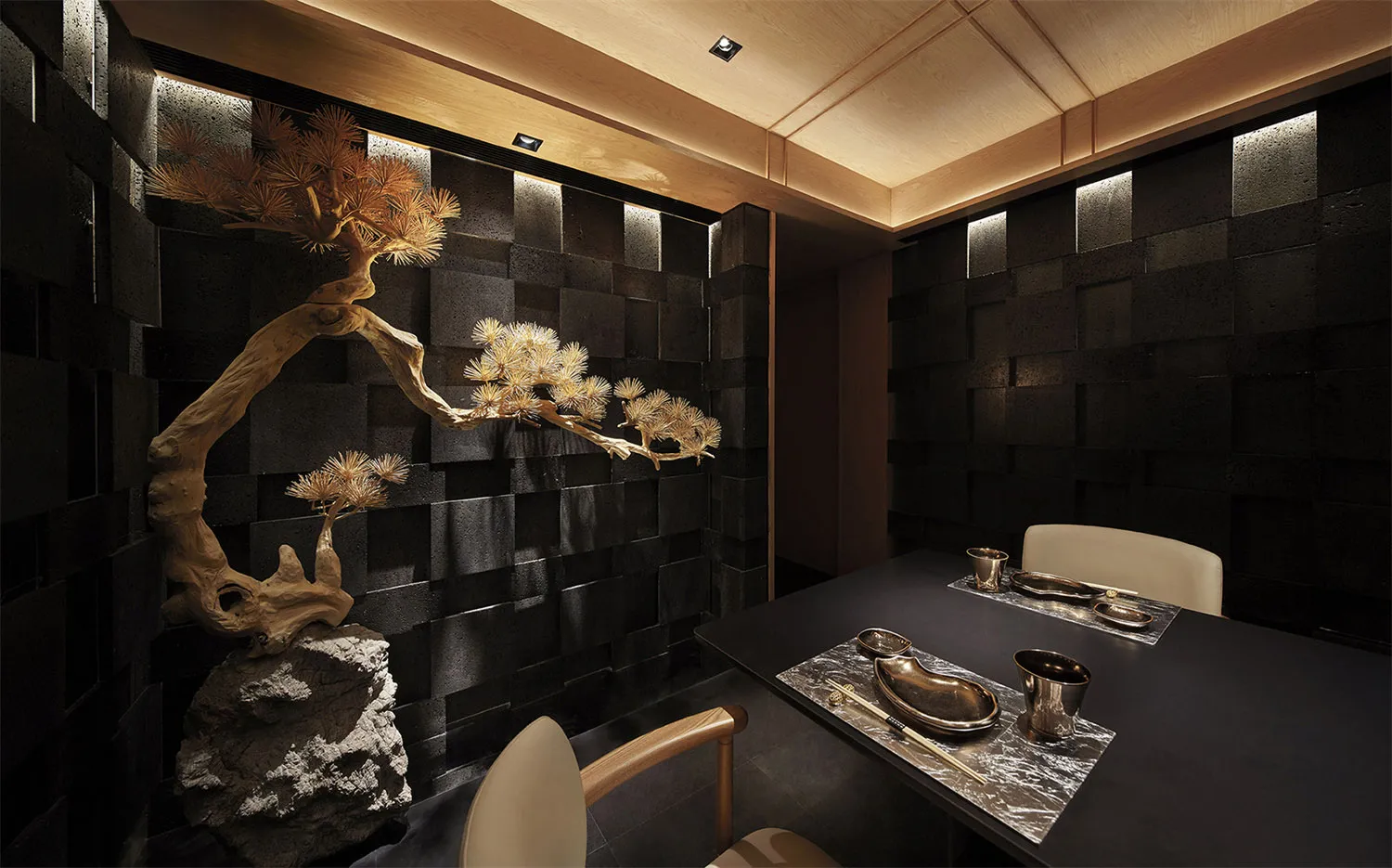 A sleek, metallic and black restaurant interior with a bonsai tree, minimalist table setting, and modern design elements.
