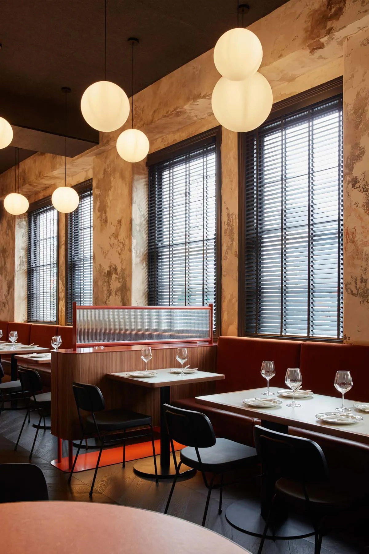 Modern cafe interior with wooden tables, velvet seating, and spherical pendant lights.