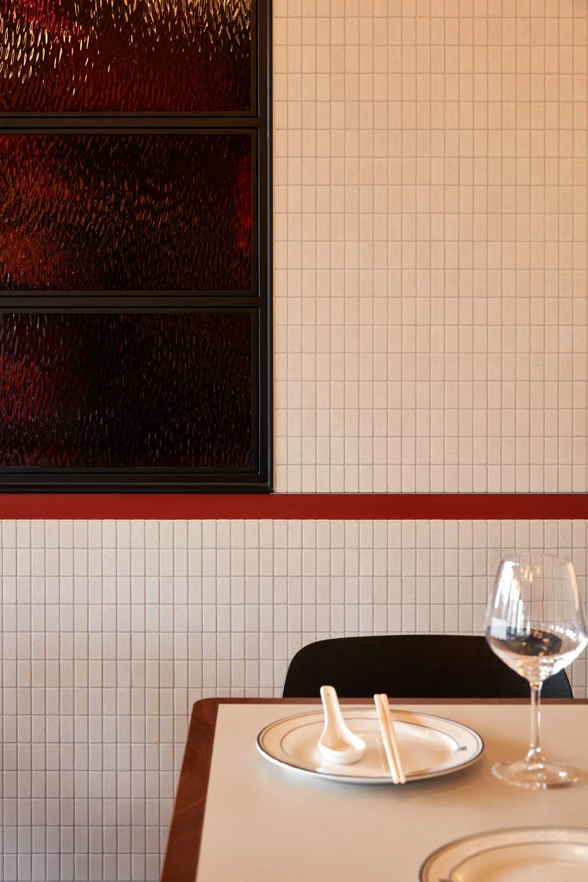 A minimalist-style restaurant interior with tile walls and a wine glass on a table.
