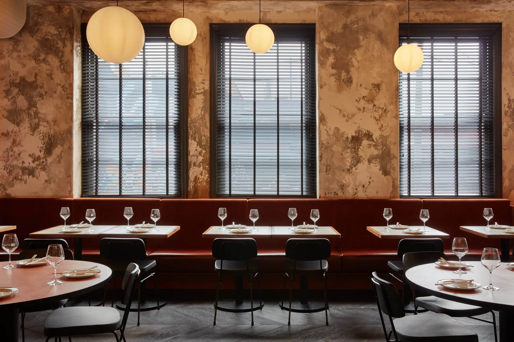 A modern restaurant interior with red leather seating and round tables.