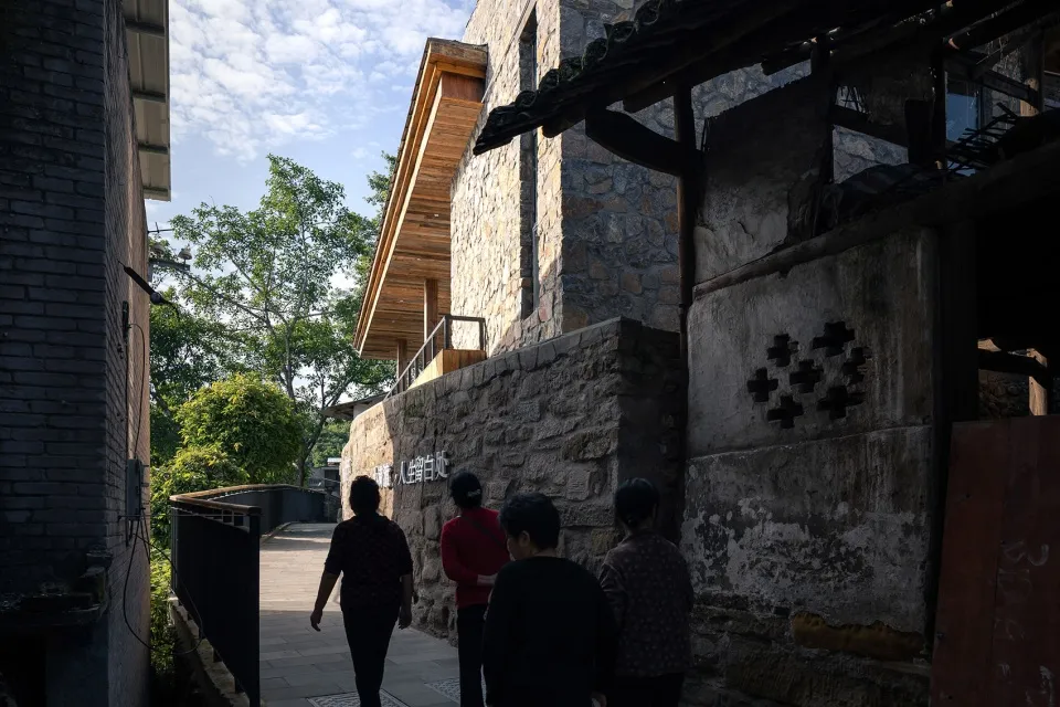 三人走在寧靜的石牆街道上，兩旁有樹木與建築物。