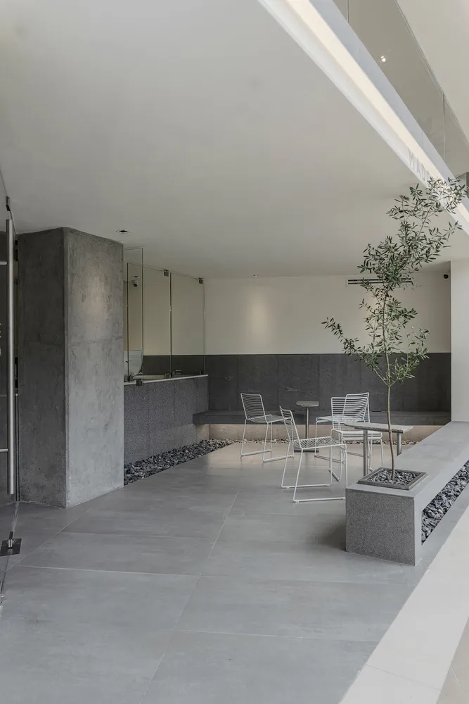 Modern, minimalist restaurant interior with concrete flooring and walls, white furniture, and greenery.