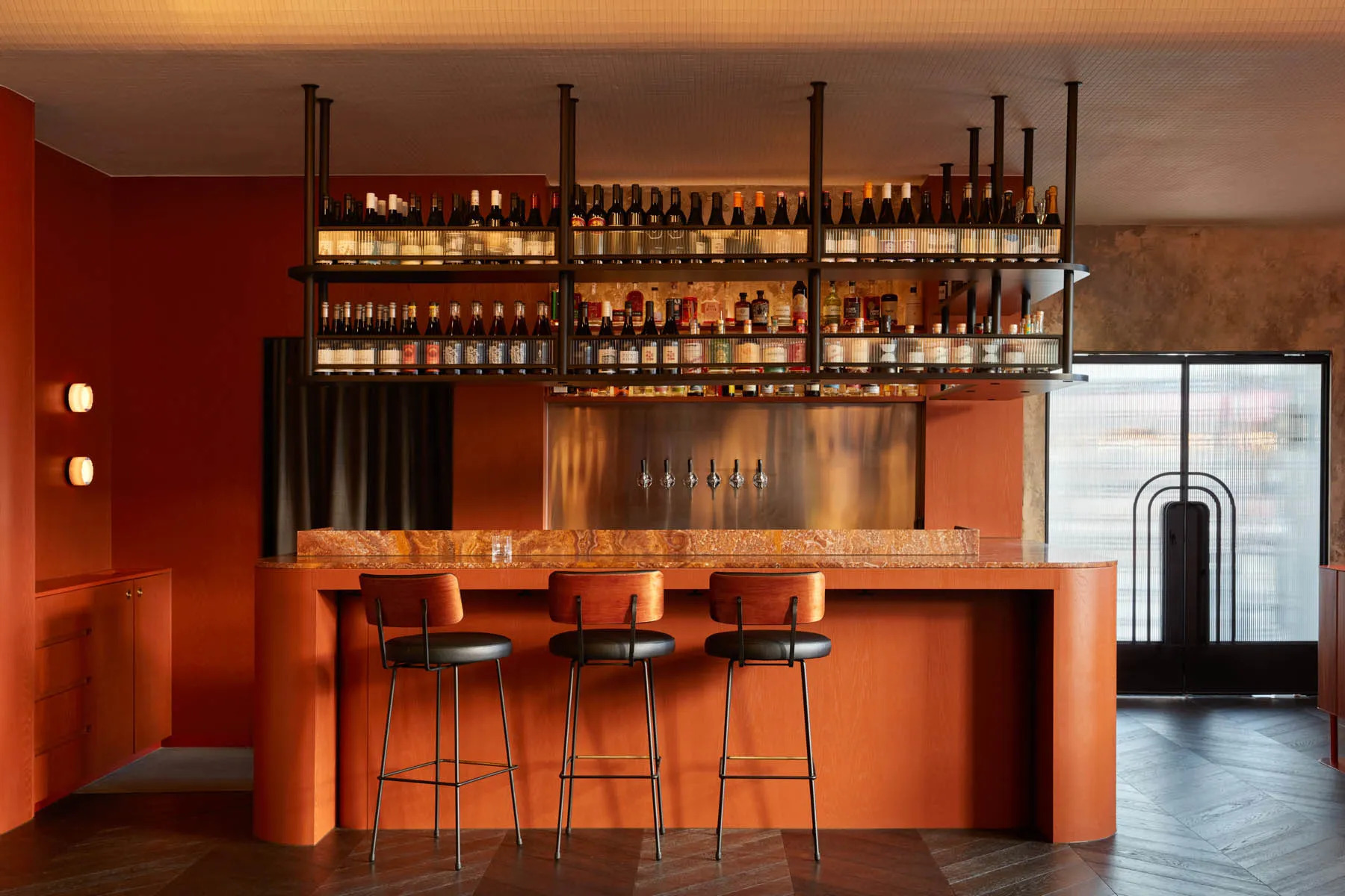 A photograph of a modern restaurant bar featuring red wooden stools and a marble countertop.