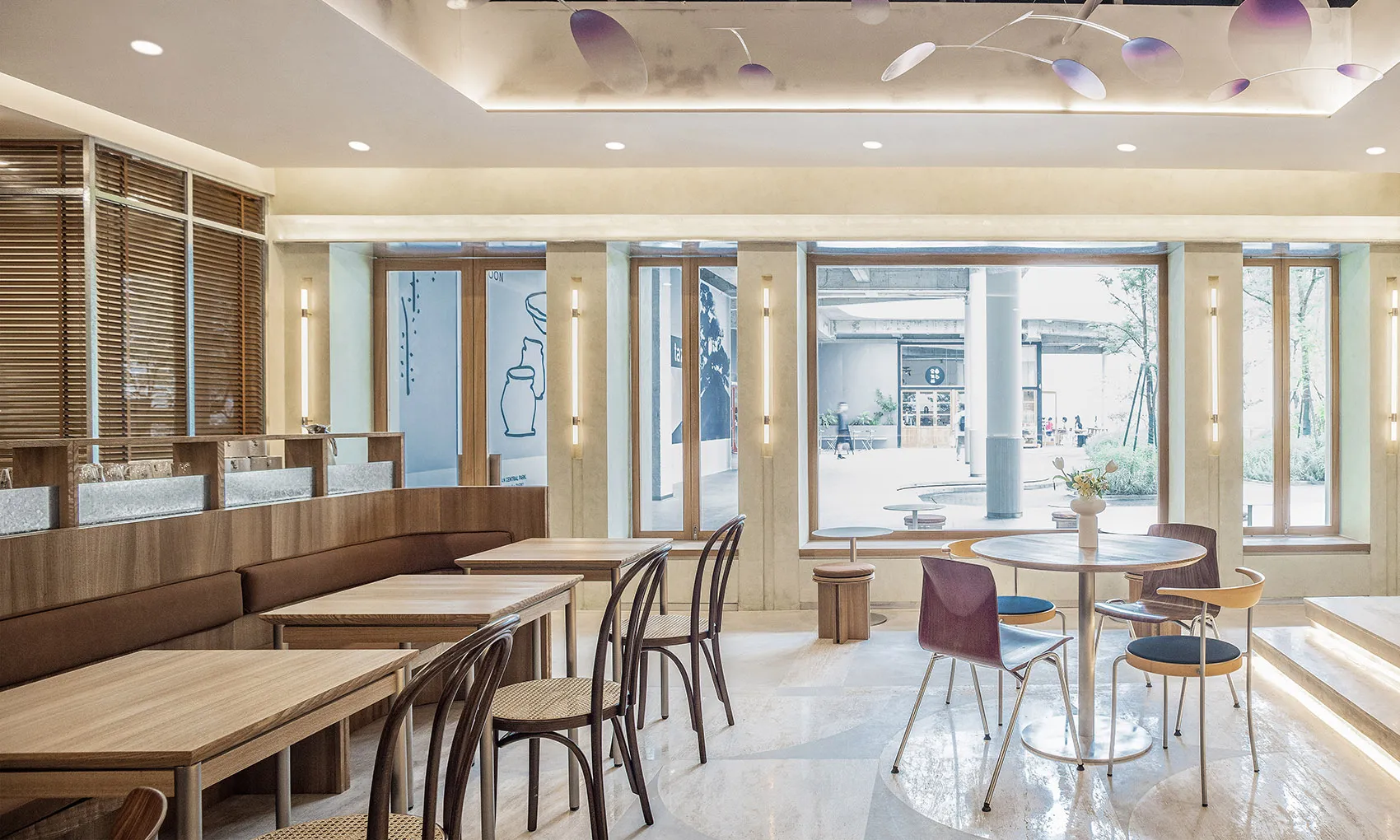 A modern cafe interior featuring wooden tables and chairs, glass partitions, and concrete flooring.