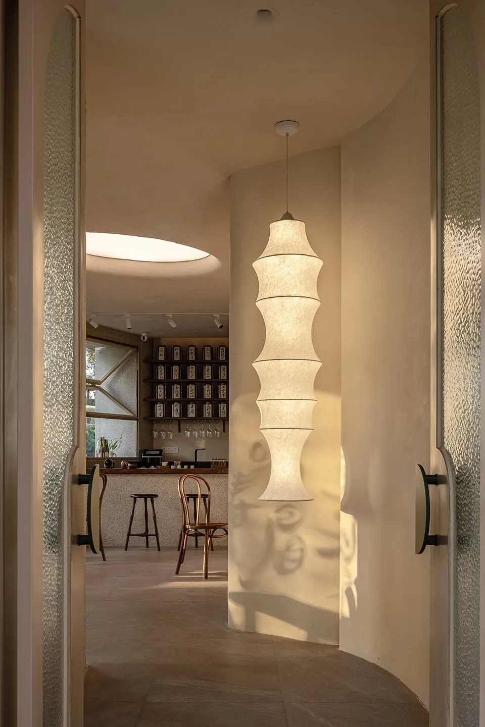 A modern bar counter with a textured wall paper and well-lit by a hanging lamp with long cylindrical white shades, creating a