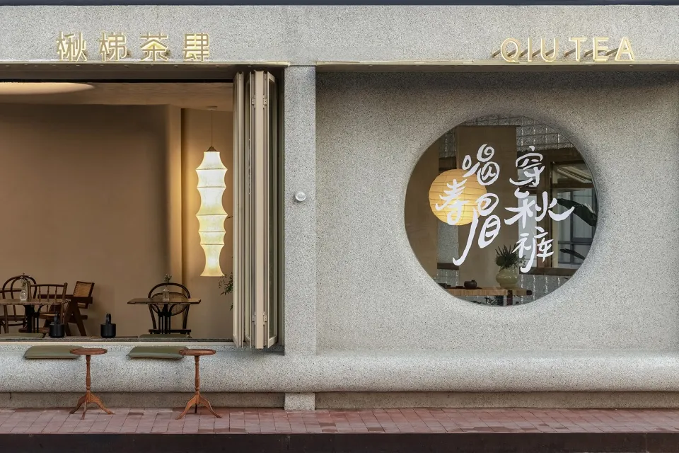 A modern coffee shop exterior with concrete walls, a large round window, and traditional lantern lighting.