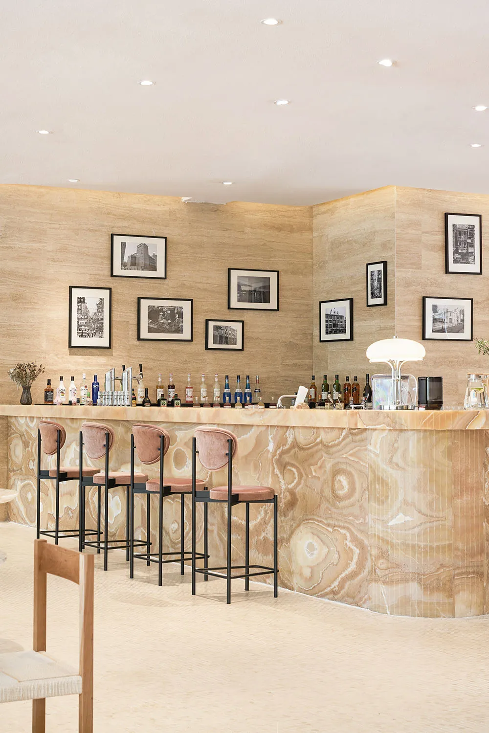 A luxurious restaurant bar with a modern design featuring a marble counter, pink velvet stools, and framed photographs on the