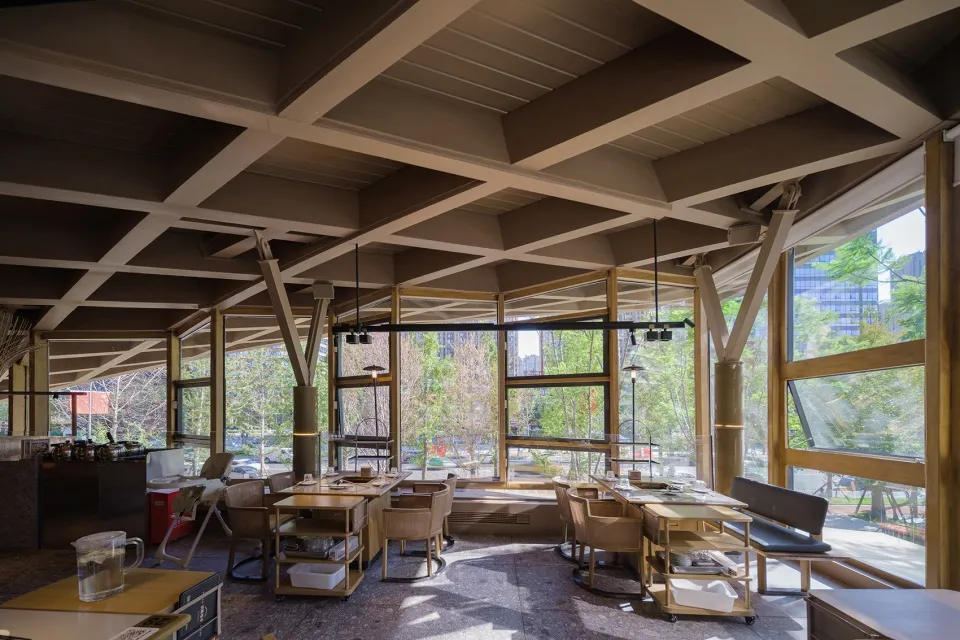 Interior of a modern restaurant with wooden furniture, glass windows, and metal columns