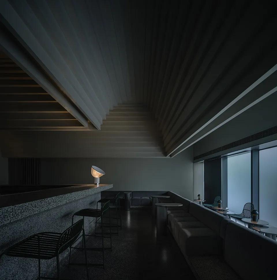 Modern cafeteria with concrete and metal interiors, featuring seating areas and lighting fixtures.