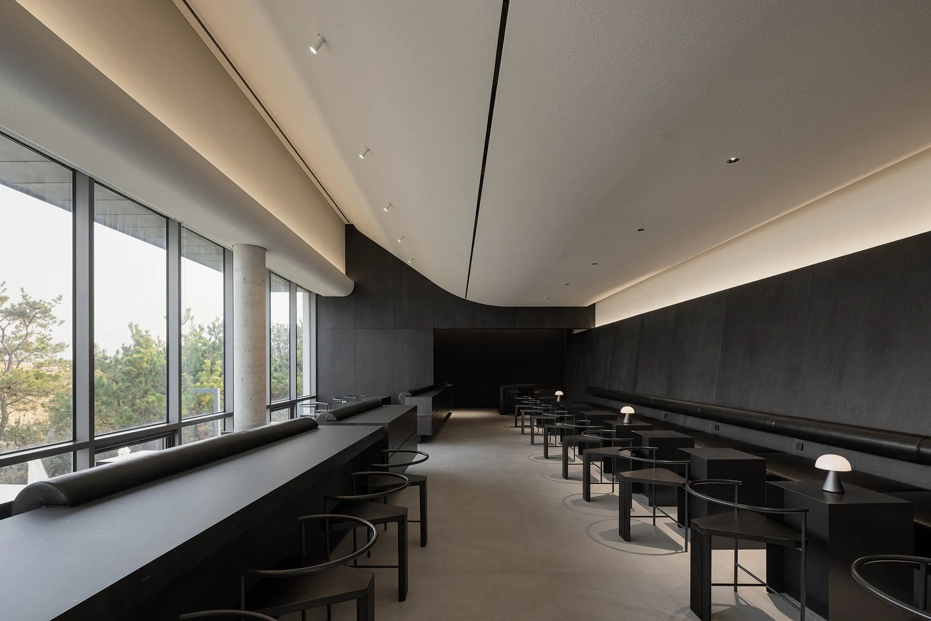 Interior of a modern restaurant with black and concrete elements, featuring minimalist design.