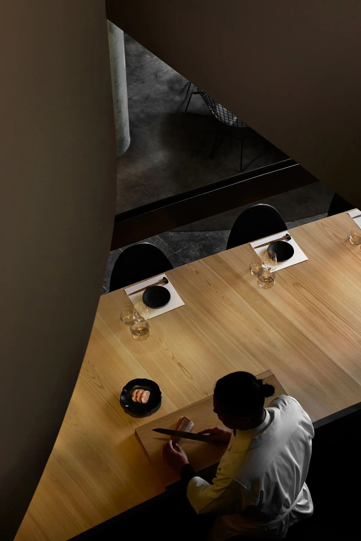 簡約風格的餐廳室內,設有木製吧台,一位廚師正在切魚。