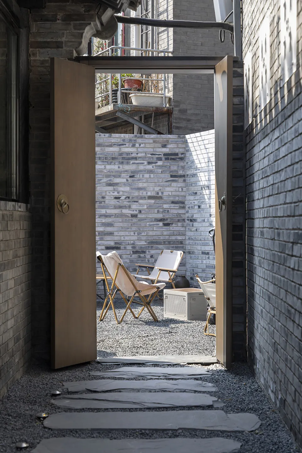 Minimalist architectural space with brick walls and a pathway leading to a seating area with chairs and a table.