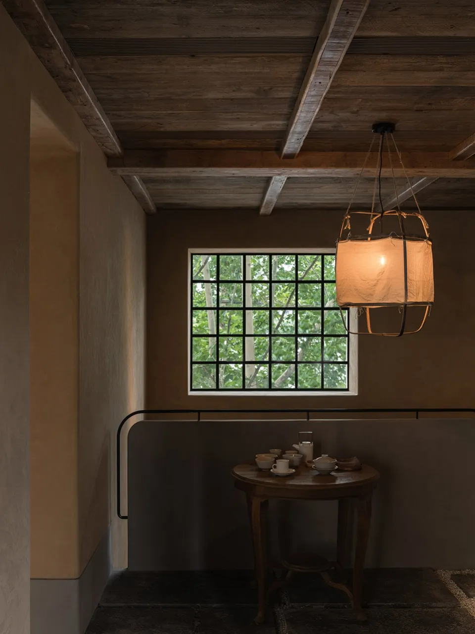 A minimalist interior design featuring a wooden window, table, and chandelier with a warm, soft light.