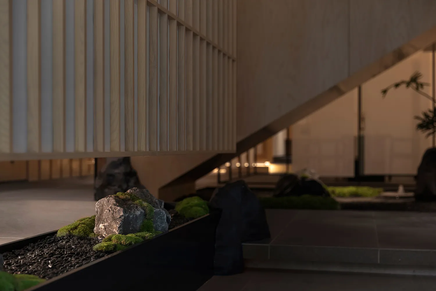 A modern bathroom featuring a rock garden with black pebbles, moss-covered rocks, and greenery, arranged in concrete surround