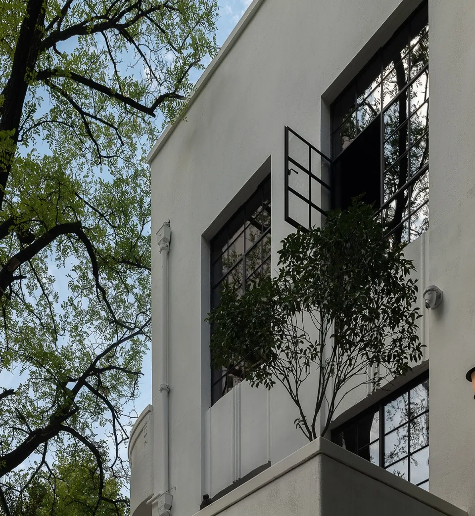 一座現代住宅建築,擁有白色混凝土外牆,搭配大片玻璃窗與綠意植栽。